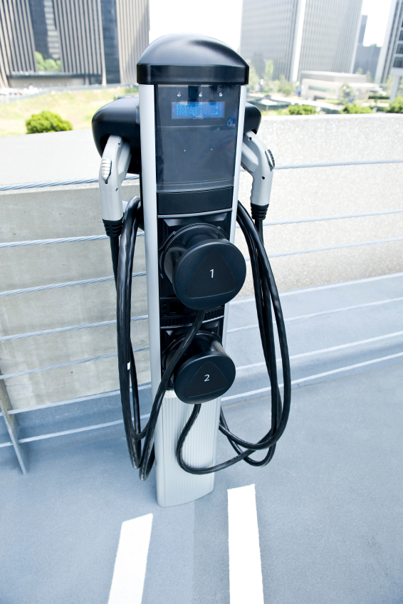 A dual electric vehicle charging station on a rooftop parking deck, with coiled charging cables hanging from the unit.