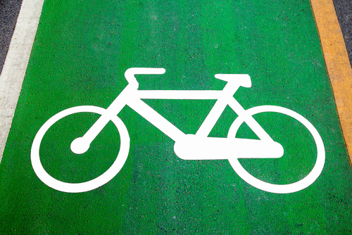 A green bicycle lane on a road marked with a white bicycle symbol. White and yellow lines border the lane.