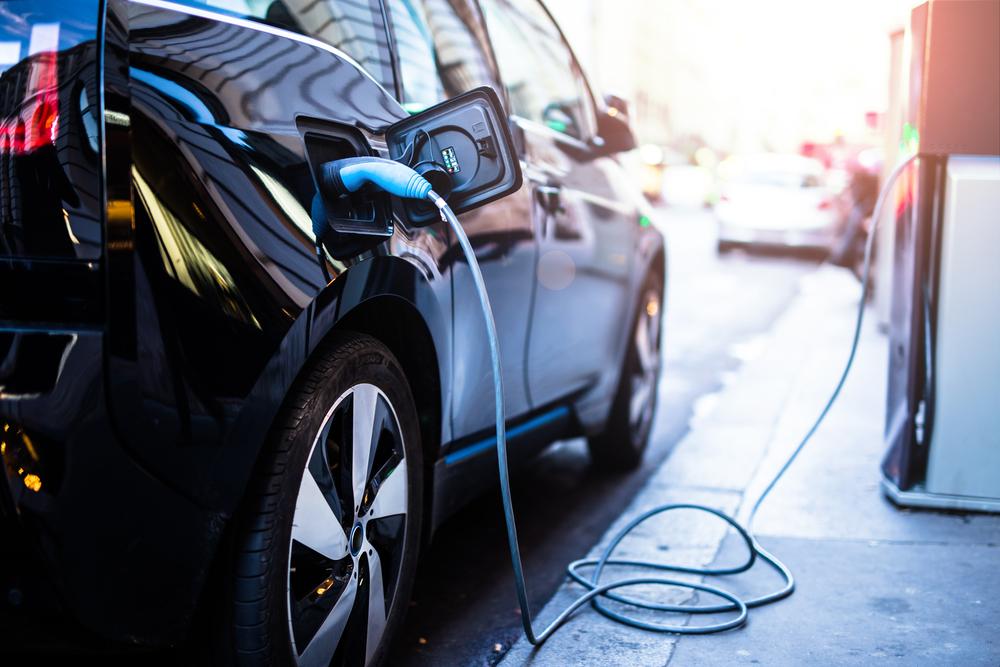 A black electric car charging at a public charging station on a city street.